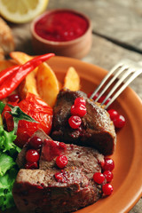 Tasty roasted meat with cranberry sauce, salad and roasted vegetables on plate, on wooden background
