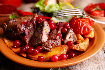 Tasty roasted meat with cranberry sauce, salad and roasted vegetables on plate, on wooden background