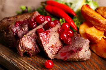 Beef with cranberry sauce, roasted potato slices on cutting board, on wooden background