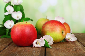 Fresh apples with apple blossom on wooden table, on nature background