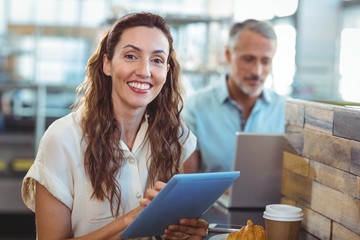 Pretty brunette smiling at camera and using tablet