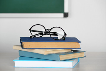 Heap of books and glasses on table in class