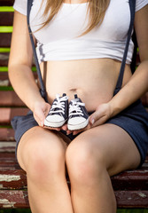 conceptual photo of pregnant woman holding baby shoes on hands