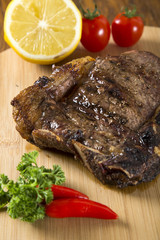 Grilled meat ribs on white plate with tomatoes chives and dark h