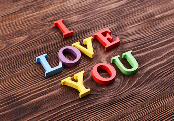 Inscription I LOVE YOU made of colorful letters on wooden background
