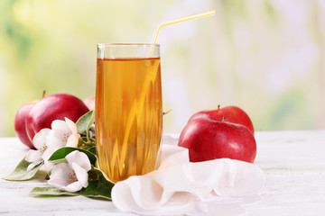 Glass of apple juice and apples on wooden table, on nature background