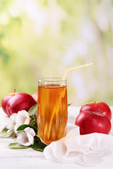 Glass of apple juice and apples on wooden table, on nature background
