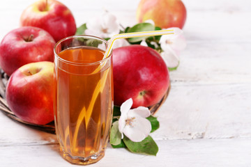 Glass of apple juice and apples on wooden table, on nature background