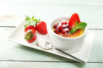 Creme brulee dessert with fresh strawberry berries on napkin, on color wooden background