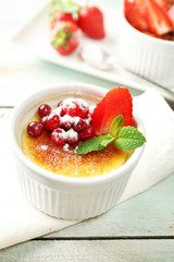Creme brulee dessert with fresh strawberry berries on napkin, on color wooden background