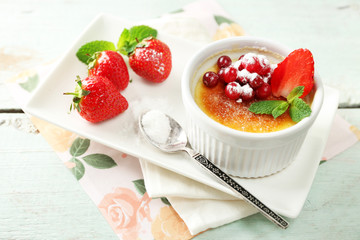 Creme brulee dessert with fresh strawberries and mint leaves, on color wooden background