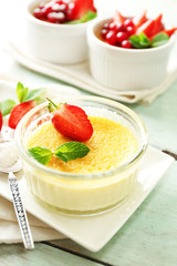 Creme brulee dessert with fresh strawberry berries on napkin, on color wooden background