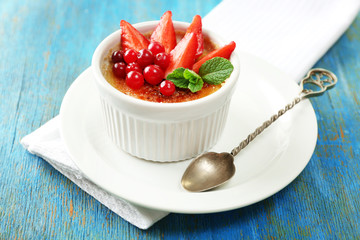 Creme brulee dessert with fresh strawberries and mint leaves, on color wooden background