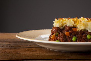 Shepherds pie shot front on on wood with grey background cropped close-up with negative space