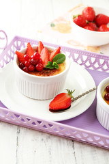 Creme brulee dessert with fresh strawberries and mint leaves, on color wooden background