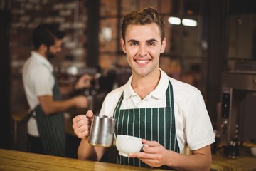 Smiling barista pouring milk in a cup