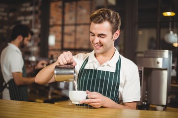 Smiling barista pouring milk in a cup