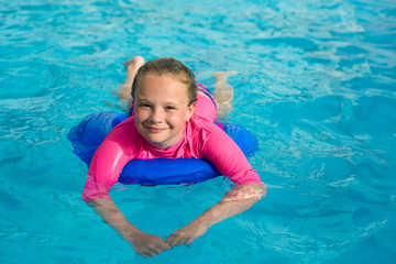 Fototapeta na wymiar Pretty little girl with blue life ring has fun in the swimming pool