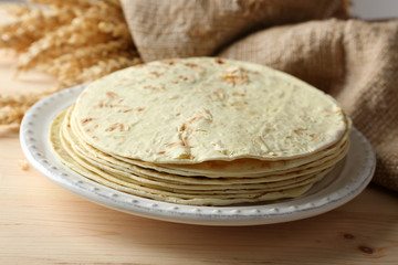 Stack of homemade whole wheat flour tortilla on plate, on wooden table background