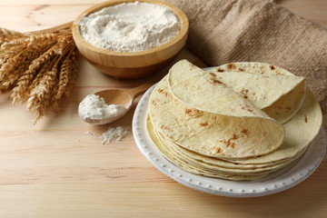 Stack of homemade whole wheat flour tortilla on plate, on wooden table background
