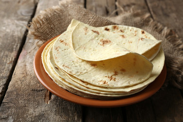 Stack of homemade whole wheat flour tortilla on plate, on wooden table background - obrazy, fototapety, plakaty
