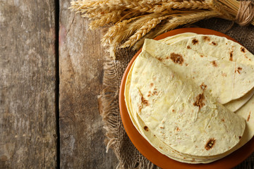 Stack of homemade whole wheat flour tortilla on plate, on wooden table background