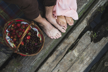 man and woman feet on wooden bridge near the basket with berries