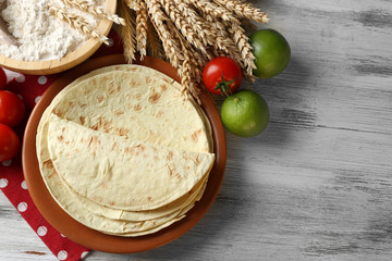 Fototapeta na wymiar Stack of homemade whole wheat flour tortilla and vegetables on plate, on wooden table background