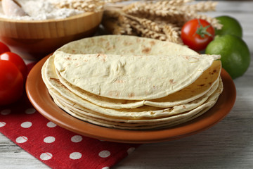 Stack of homemade whole wheat flour tortilla and vegetables on plate, on wooden table background