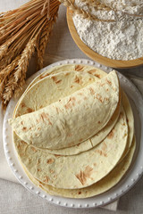 Stack of homemade whole wheat flour tortilla on napkin, on light background