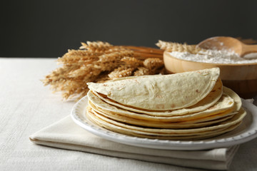 Stack of homemade whole wheat flour tortilla on plate, on dark background