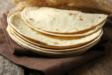 Stack of homemade whole wheat flour tortilla on napkin, on wooden background