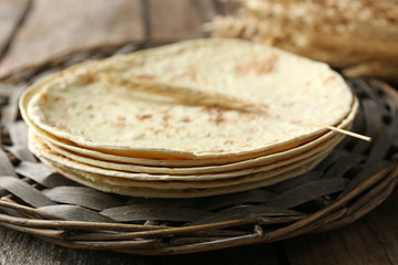 Stack of homemade whole wheat flour tortilla on wicker mat, on wooden background