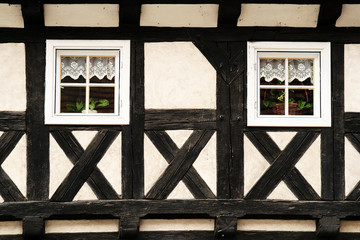 White half-timbered wall with two white windows, old city of Zgorzelec, Poland. In the window curtains and flowers 