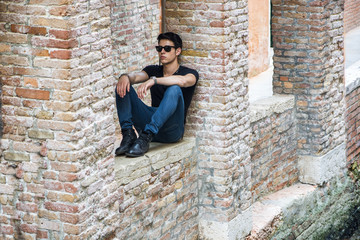 Attractive young man sitting against brick wall