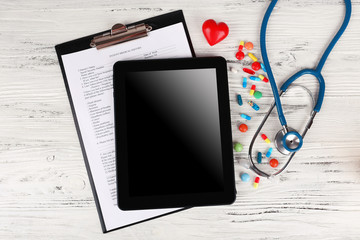 Tablet with blue stethoscope and tablets on wooden background