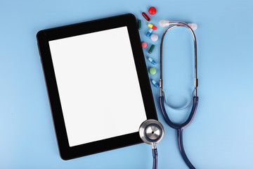 Tablet with stethoscope and tablets on blue background