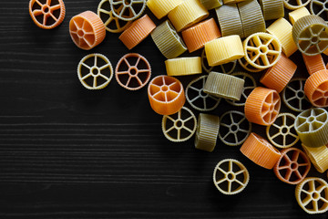 Dry coloured wagon wheel pasta on black textured wood, from abov