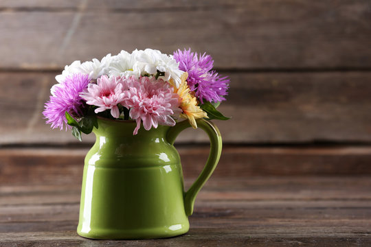 Beautiful chrysanthemums in pitcher on wooden background