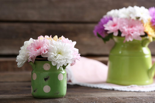 Beautiful chrysanthemums in pitchers on wooden background