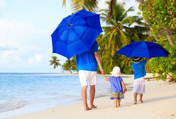 Father and kids at beach with umbrellas to hide from sun