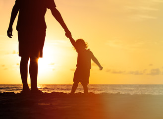 silhouettes of father and little daughter walking at sunset