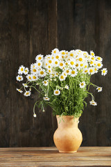 Beautiful bouquet of daisies in pitcher on wooden background