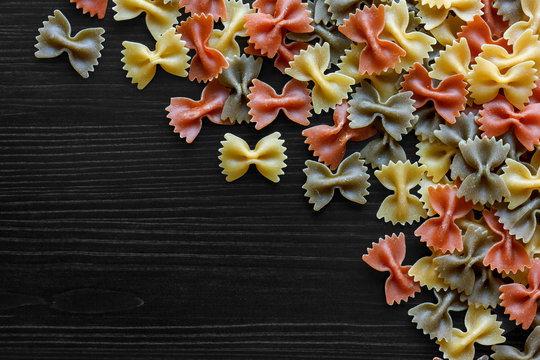 Dry Coloured Farfalle Pasta On Black Textured Wood From Above. S