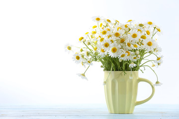 Beautiful bouquet of daisies in cup on light background