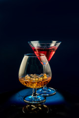 Two glasses of alcohol on a black background, red martini and cognac