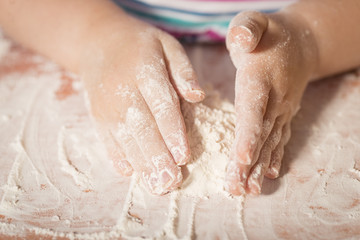 Little chef hands smeary with flour playing with dough