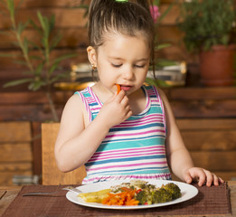Little girl eating by itself broccoli, carrot and bell paper with hands
