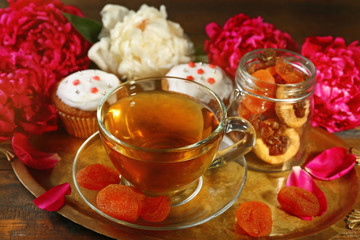 Composition with cup of herbal tea, dried apricots and peony flowers on wooden background