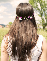 Naklejka premium Beautiful long woman's hair with the flower in the head, standing in the meadow